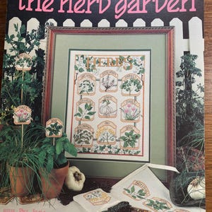 Può includere: Un modello a punto croce intitolato "the herb garden" con varie erbe, tra cui origano, rosmarino e prezzemolo. Il disegno è incorniciato e presentato con erbe in vaso e accessori correlati. Il libretto è di Leisure Arts.