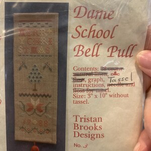 May include: A cross-stitch kit for a bell pull, featuring a tan fabric with a Christmas design. The design includes a Christmas tree, floral elements, and the text "MERRY CHRISTMAS". The kit includes a tassel and measures 3 inches by 10 inches.