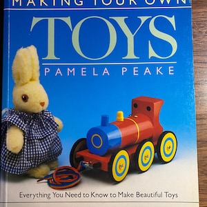 May include: A book cover titled "MAKING YOUR OWN TOYS" by Pamela Peake. The cover features a yellow stuffed bunny wearing a blue and white checkered dress, and a red, blue, and yellow toy train. The text below reads "Everything You Need to Know to Make Beautiful Toys".