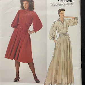 May include: Vogue Patterns Designer Original sewing pattern for a dress by Jean Muir. The pattern is for a long, flowing dress with a gathered waist and a V-neckline. The pattern is shown on two models, one wearing a red dress and the other wearing a beige dress. The pattern number is 2997.