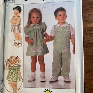 May include: Simplicity sewing pattern 9497 for children's clothing. The pattern includes instructions for a girl's dress with a Peter Pan collar and a boy's dungarees with a plaid pattern.