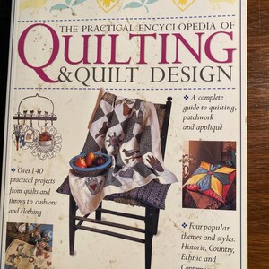 May include: The Practical Encyclopedia of Quilting & Quilt Design book cover features a colorful quilt on a wooden chair, a basket of fruit, and a pillow. The book title is in large, bold letters. The book cover also includes text about the book's contents, including over 140 projects, a complete guide to quilting, patchwork, and appliqué, and four popular themes and styles: Historic, Country, Ethnic, and Contemporary.