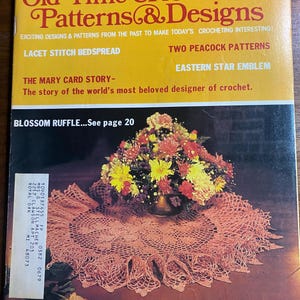 Puede incluir: Una portada de revista vintage del verano de 1980, titulada "Old Time Crochet Patterns & Designs". Muestra un tapete de ganchillo color melocotón con un arreglo floral. El texto incluye "Lacet Stitch Bedspread" y "Blossom Ruffle".