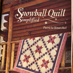 May include: A book titled "Snowball Quilt Simplified" by Patricia Knoechel, featuring a quilt with a red, white, and blue star pattern against a white background. The book cover also shows a wooden cabin with icicles hanging from the roof.