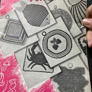 Pode incluir: Uma capa de livro vintage que apresenta uma coleção de pegadores de panela de crochê em várias formas e designs, incluindo um peixe, um caranguejo, uma flor e uma folha. A capa do livro é rosa com o título "Star Potholders" impresso em preto.