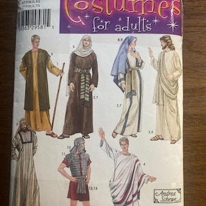 Op de afbeelding: Simplicity kostuum patroon voor volwassenen. De verpakking toont illustraties van historische kostuums, waaronder Romeinse, bijbelse en middeleeuwse kleding. Het kleurenpalet omvat beige, bruin en wit, met accenten van rood en blauw. Het patroon bevat maten XS tot XL.