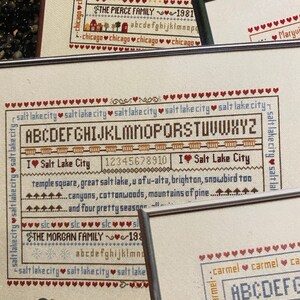Peut inclure: Deux broderies au point de croix, l'une pour Chicago et l'autre pour Salt Lake City. Les deux motifs présentent le nom de la ville, un cœur et l'alphabet. Le motif de Chicago comprend également le texte "the lights and excitement make me feel alive, high towering buildings, bustling nine to five charming shops and theatre-on these" et "THE PIERCE FAMILY 1981". Le motif de Salt Lake City comprend le texte "temple square, great salt lake, u of u-alta, brighton, snowbird too canyons, cottonwoods, mountains of pine... and four pretty seasons..." et "THE MORGAN FAMILY 198".