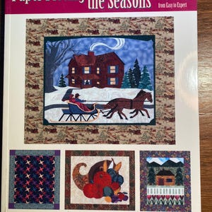 May include: Book cover for "Paper Piecing the Seasons" by Liz Schwartz & Stephen Seifert. The cover features a winter scene with a house, a horse-drawn sleigh, and a snowy landscape. The book is part of the "That Patchwork Place" series and focuses on foundation piecing techniques.