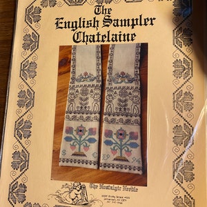 Pode incluir: Um padrão para um projeto de ponto cruz de Chatelaine de Sampler inglês. O padrão apresenta dois painéis bordados com motivos florais e uma borda de folhas estilizadas. O padrão é de The Nostalgic Needle, 20200 Shirley Trace #201, Germantown, MD 20874, 301-540-4466.