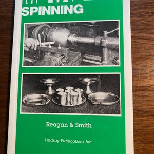 May include: A green book titled "Metal Spinning" with a black and white photo of a metal spinning lathe on the front cover. The book also features a black and white photo of a collection of metal bowls and cups. The book is published by Reagan & Smith, Lindsay Publications Inc.