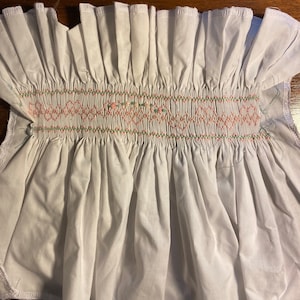 Puede incluir: Tela de algodón blanca con un borde rizado y una banda de bordado rosa y verde.