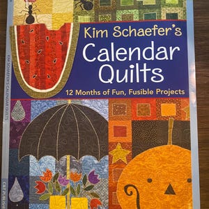 May include: A quilting pattern book titled "Kim Schaefer's Calendar Quilts" with colorful quilt block designs. The cover features a watermelon, umbrella, and pumpkin. Includes an instruction booklet and full-size patterns for 12 months of fusible projects.