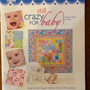 Puede incluir: Un libro titulado "Still Crazy for Baby" con una portada azul y un borde blanco. La portada presenta un bebé, una colcha y una silla de mimbre blanca. El libro es de Me & My Sister Designs, Barbara Groves & Mary Jacobson. Incluye 4 colchas rápidas para bebés.