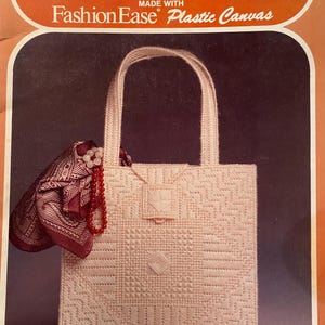 May include: A light pink tote bag made with plastic canvas, featuring a geometric design. A maroon scarf and a beaded necklace are draped over the bag. The text "Fashion Accessory Ideas" and "Fashion Ease Plastic Canvas" are visible.