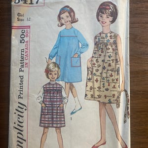 Könnte beinhalten: Vintage Simplicity-Druckmusterumschlag. Der Umschlag zeigt Illustrationen von drei Mädchen, die Kleider tragen. Das Muster ist für eine Mädchengröße 12. Der Umschlag hat die Nummer 5417 und den Preis von 50c in Kanada.