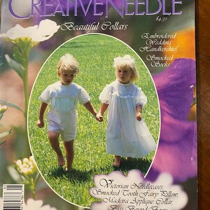 May include: A magazine cover featuring two children in white dresses and a white shirt walking in a grassy field. The magazine is called "Creative Needle" and the cover text says "Beautiful Collars". The cover also features a list of projects including "Embroidered Wedding Handkerchief, Smocked Socks, Victorian Needlecases, Smocked Tooth Fairy Pillow, Madeira Applique Collar, Bias Bound Bows".