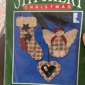 May include: A craft kit for making three Christmas ornaments. The kit includes stamped natural muslin fabric, batting, fusible webbing, buttons, pearl cotton, and floss. The ornaments are a stocking, an angel, and a heart. The kit is by Bernat and the kit number is 95-6002-00.