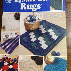 May include: A book cover for "Big Needle Knit Rugs" by Annie's Attic, showcasing various knitted rug designs. The images display rugs in diverse colours and patterns, such as blue, white, and red. A basket of yarn balls is also visible.