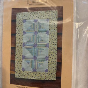 May include: A paper foundation pattern for a quilt runner called "Spring Colorado Log Cabin Runner". The pattern is 14 inches by 22 1/4 inches and is designed by MH Designs. The pattern number is MH636.