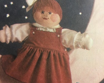 May include: A handmade doll with red hair, a white bow, and a brown dress with white stars. The doll is standing on a crescent moon with a starry background.
