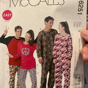 May include: McCall's M6251 sewing pattern featuring pajama designs. The pattern includes options for a red and black top with patterned pants, a red top with a peace sign and patterned pants, a brown jumpsuit, and a red heart-patterned jumpsuit.