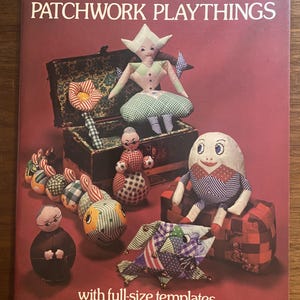 May include: A softcover book titled Margaret Hutchings Patchwork Playthings with full-size templates. The cover features a collection of handmade fabric dolls, a segmented caterpillar toy, and a fish toy arranged around a small open trunk.