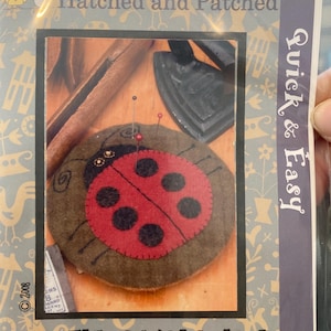 May include: A packaged craft kit labeled "Hatched and Patched" featuring a ladybug pincushion. The pincushion is brown with a red and black ladybug design. The text "Doug the Bug Pincushion" is visible. The package also says "Quick & Easy".