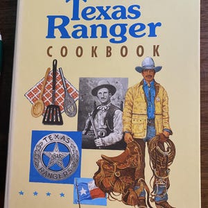 May include: A hardcover book titled The Authorized Texas Ranger Cookbook with a light yellow cover. The cover features a vintage photograph of a ranger, a Texas Ranger star badge, a Texas flag, kitchen utensils, and an illustration of a ranger.