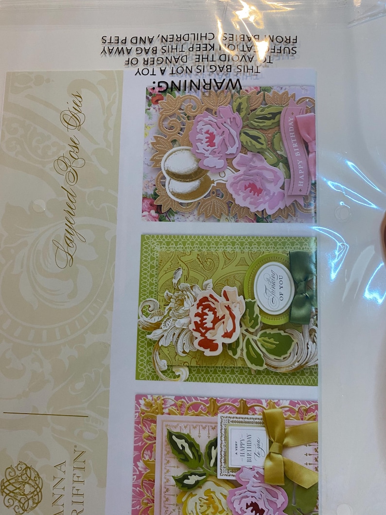 Może przedstawiać: Opakowanie warstwowych wykrojnik&oacute;w r&oacute;ż do rękodzieła. Obraz przedstawia trzy przykładowe projekty kart z kompozycjami kwiatowymi, w tym r&oacute;żowe i ż&oacute;łte r&oacute;że, dekoracyjne ramki oraz tekst "Happy Birthday" i "Thinking of You".