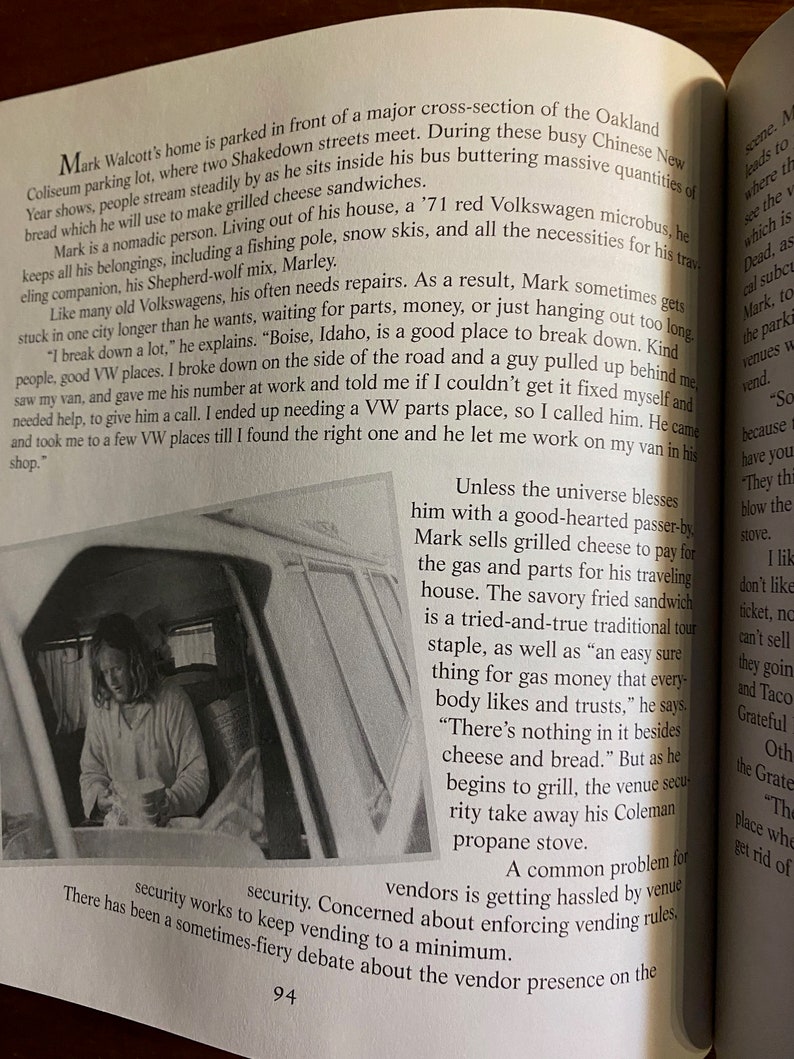 Puede incluir: Una fotograf&iacute;a en blanco y negro de un hombre sentado en una camioneta, sosteniendo una taza. El texto "Unless the universe blesses him with a good-hearted passer-by Mark sells grilled cheese to pay for the gas and parts for his travelling house. The savoury fried sandwich is a tried-and-true traditional tour staple, as well as "an easy sure thing for gas money that everybody likes and trusts," he says. "There's nothing in it besides cheese and bread." But as he begins to grill, the venue security take away his Coleman propane stove." es visible en la imagen.