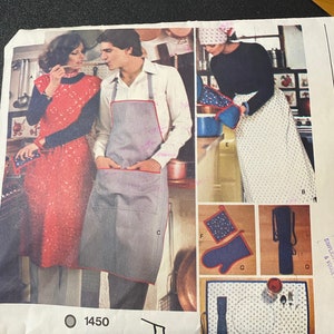 May include: A vintage sewing pattern for a pair of aprons and kitchen accessories. The pattern includes instructions for a blue and white striped apron, a red and white floral apron, a blue oven mitt, a blue pot holder, a blue and white striped placemat, and a blue and white striped utensil holder. The pattern number is 1450.