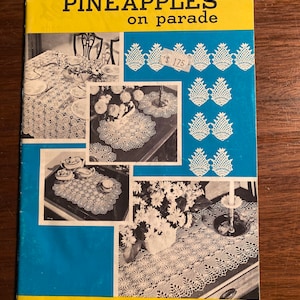 Könnte beinhalten: Ein Vintage-Häkelmusterbuch mit dem Titel "Pineapple on Parade" von Coats Book No. 96. Das Buch zeigt Fotos von gehäkelten Ananas-Mustern für Tischdecken, Deckchen und Platzsets.
