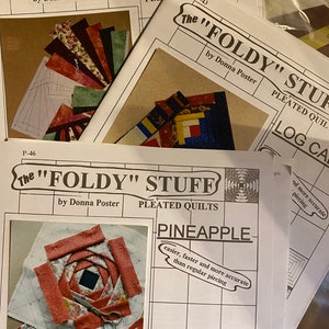 May include: A stack of quilting pattern booklets titled "The Foldy Stuff" by Donna Poster. The booklets feature images of quilt blocks and the word "Pineapple". The text on the booklet says "easier, faster and more accurate than regular piecing."