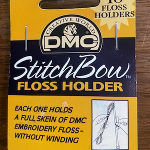 May include: A package of DMC Stitch Bow floss holders. The package is yellow and navy blue, with the DMC logo and the text "10 Floss Holders." The text "Stitch Bow Floss Holder" is also visible. The package states each holder holds a full skein of embroidery floss.