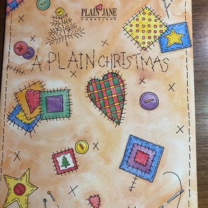 May include: A watercolor illustration of a Christmas themed patchwork quilt with a red heart, a green and red heart, a blue star, a green tree, and a red and purple square. The quilt is surrounded by stitching, buttons, and pins. The text "A PLAIN CHRISTMAS" is written in brown lettering on the quilt. The text "PLAIN JANE CREATIONS" is written in brown lettering on the quilt.