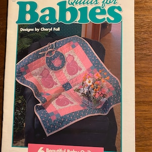 May include: A book titled "Quilts for Babies" with a pink and blue baby quilt on the cover. The book features 6 beautiful baby quilts you'll love to appliqué. Designs by Cheryl Fall.