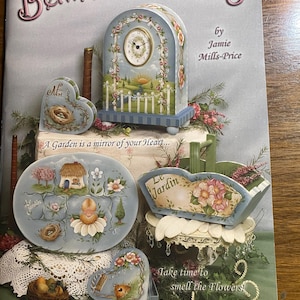 May include: A book cover titled "Between the Vines 8" with painted decorative items. A clock, heart-shaped box, and other items are painted with floral and garden themes. The text "Take time to smell the Flowers!" is visible.