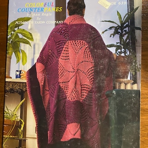 May include: A knitting pattern book titled "Colorful Counterpanes" by Ann Regis for Plymouth Yarn Company. The cover features a woman wearing a knitted shawl in shades of pink and purple.