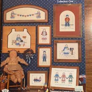 May include: A book titled "Prairie Friends Collection One" by Canterbury Designs features cross-stitch patterns with a country theme. The book cover shows a variety of cross-stitch designs, including a couple holding hands, a child holding a teddy bear, a woman sewing, and a family of three holding hands. The book cover also includes the text "Designed for Canterbury Designs by Kristy Goodin Soard" and the number "93538".