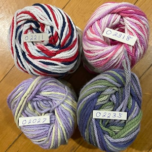 May include: Four balls of yarn in different color combinations. The yarn is white with red, blue, and white stripes, white with pink and purple stripes, purple with yellow stripes, and blue with green and purple stripes. Each ball has a handwritten label with a number: 02211, 02318, 02027, and 02235.