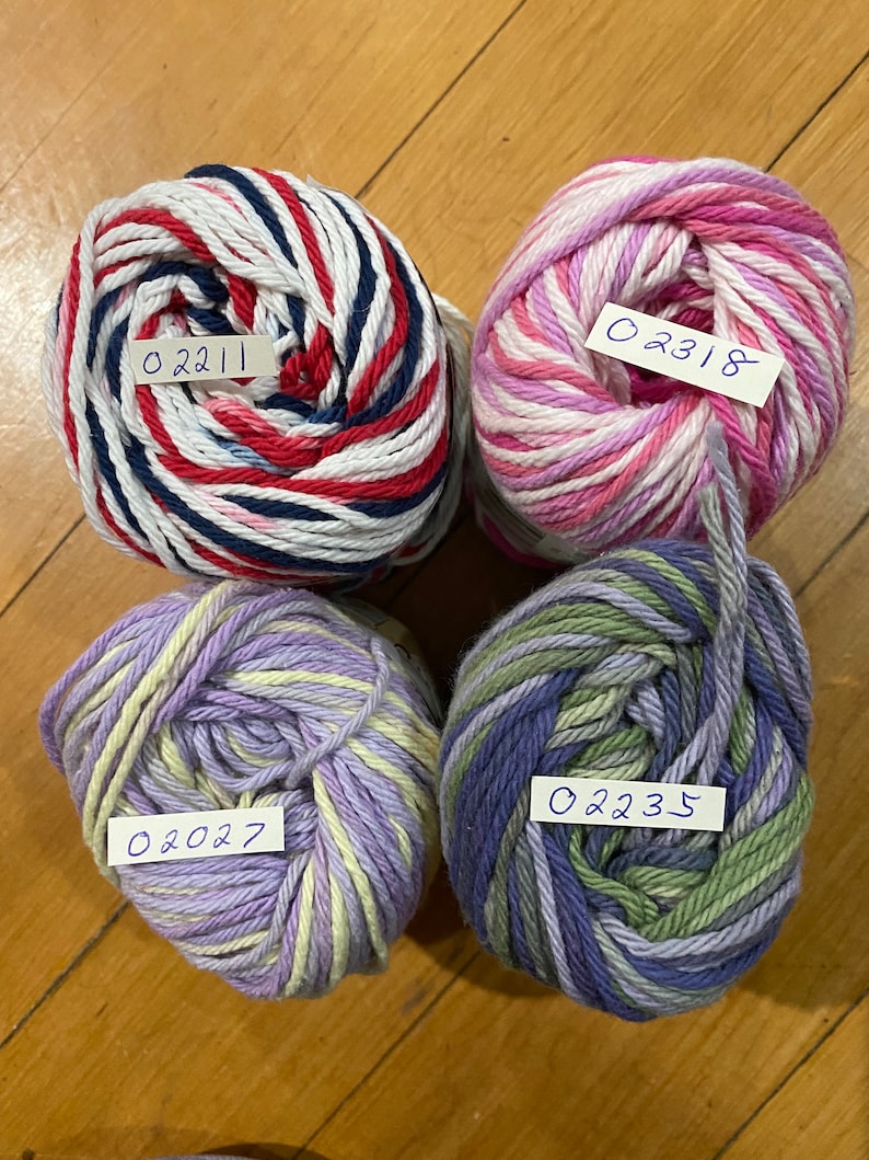 May include: Four balls of yarn in different color combinations. The yarn is white with red, blue, and white stripes, white with pink and purple stripes, purple with yellow stripes, and blue with green and purple stripes. Each ball has a handwritten label with a number: 02211, 02318, 02027, and 02235.