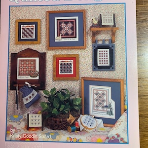 May include: A pink book cover titled "Quilted Delights" features framed cross-stitch samplers in various designs. The cover includes the text "by Kristy Goodin Soard" and "GRAPH-IT ARTS". The samplers are in wooden frames.