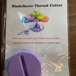 May include: A purple BladeSaver Thread Cutter with a circular design and a slot for cutting threads. The packaging includes the text "Purple Hobbies LLC" and "BladeSaver Thread Cutter". The image also shows colorful thread cutter discs.