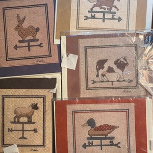 Peut inclure: Ensemble de cinq motifs de point de croix représentant différents animaux sur une girouette. Les animaux comprennent un lapin, un cheval, une vache, un mouton et un canard. Chaque motif est encadré dans un carton brun, rouge ou beige.