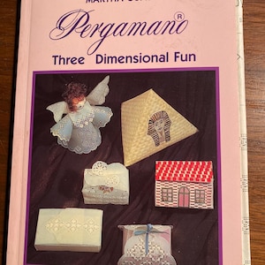May include: A book titled "Pergamano Three Dimensional Fun" by Martha Ospina. The cover features a pink background with a white angel, a pyramid, a house, and three boxes.