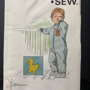 Può includere: Un pacchetto di modelli Kwik Sew vintage, modello 854, con un'illustrazione di un bambino in tuta azzurra con un'applicazione a forma di orsetto. Il pacchetto include il testo "TRANSFER INCLUDED" ed è progettato per le età 1-2-3.