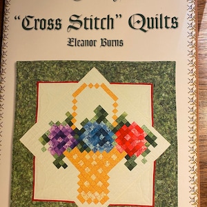 May include: A quilt pattern book titled "Cross Stitch" Quilts by Eleanor Burns. The cover features a green and white quilt with a basket of flowers in the center.
