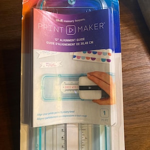 Può includere: Una guida all'allineamento Print Maker We R Memory Keepers da 30,48 cm in confezione di plastica trasparente. Il prodotto presenta una cornice blu con un righello stampato che mostra le misure in pollici e centimetri per l'allineamento.