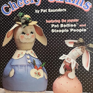 Puede incluir: Portada de libro con el título "Cheery Chums" y dos figuras de conejos pintados. Los conejos llevan sombreros y vestidos. El fondo es un patrón de puntos oscuros. El libro es de Pat Saunders.