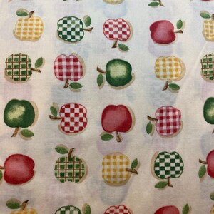 May include: A white fabric with a repeating pattern of red, green, and yellow apples. The apples have different patterns, including checkered, plaid, and solid colours.